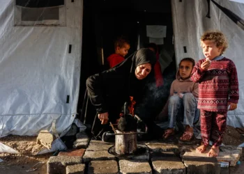 Una mujer calienta algo para comer en un campamento en Gaza/AFP